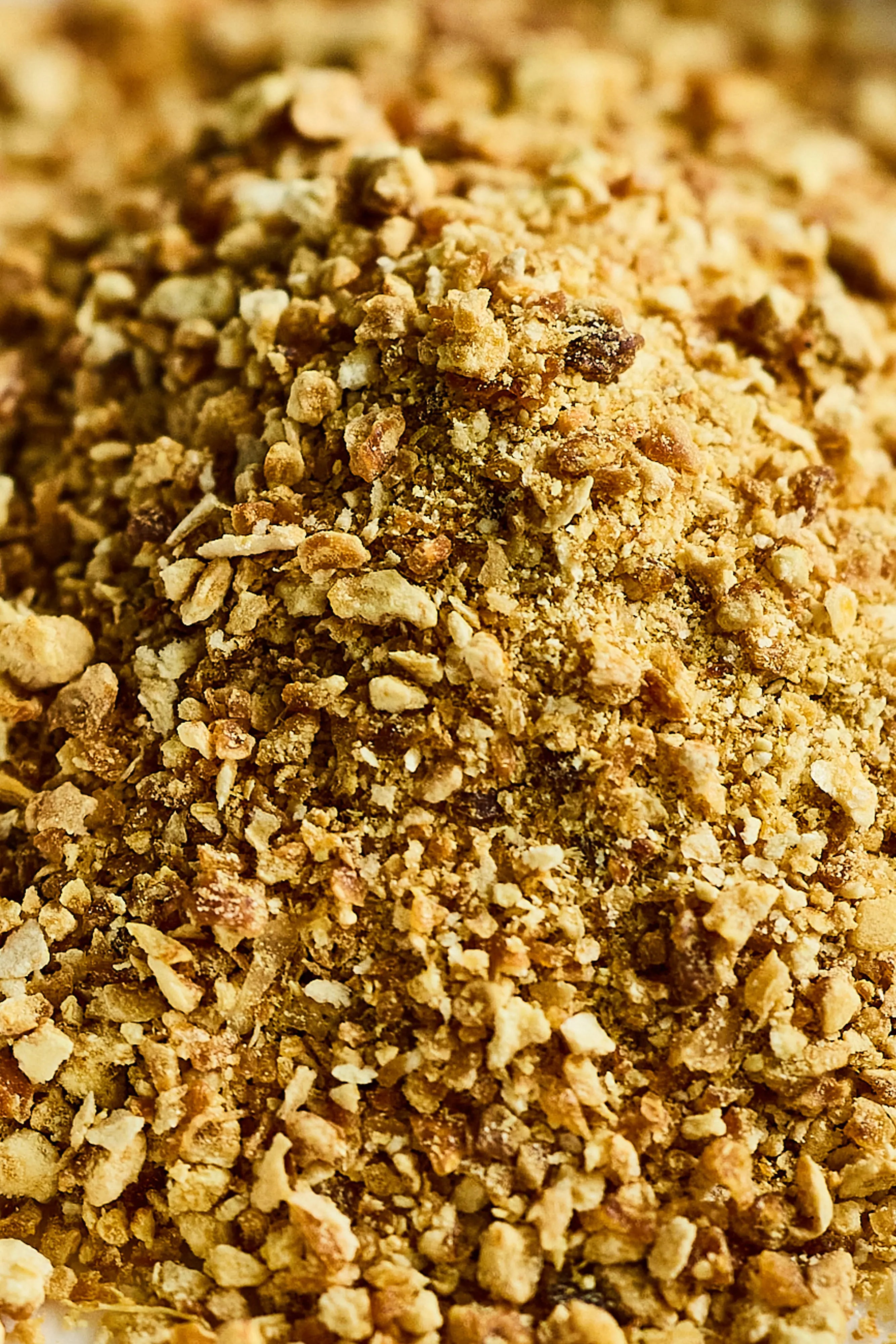 A close-up view of finely ground yuzu powder in loose, uneven granules ranging from pale yellow to light brown, creating a coarse, crumbly texture.