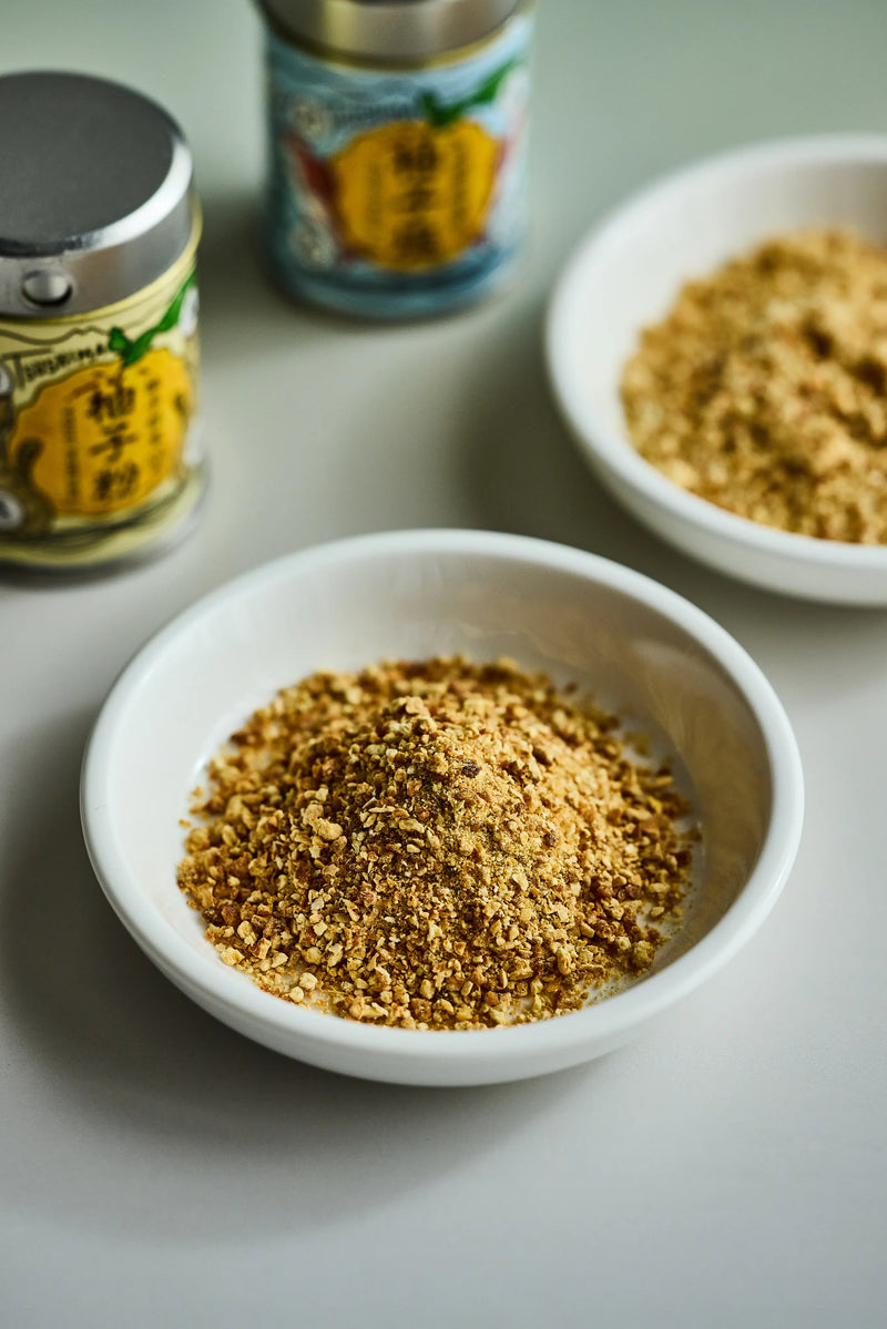 Two bowls of ground spice on a light surface with two containers in the background.
