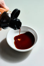 Kaneyoshi Dashi Shoyu pouring into a white dish on a gray background.