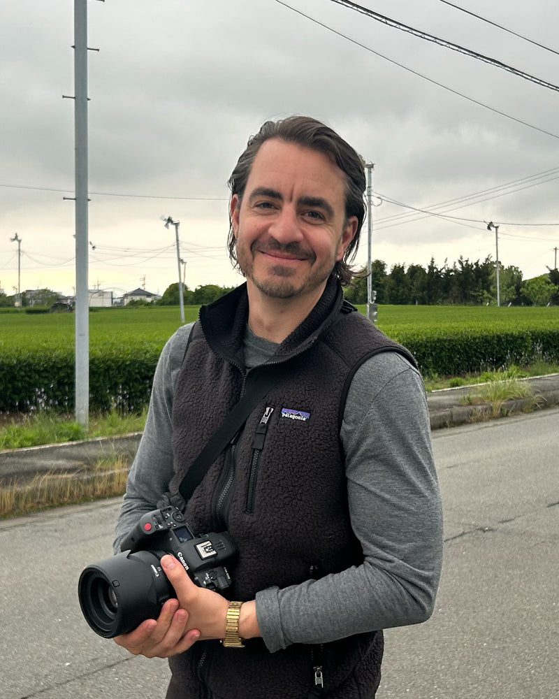 Eric holding a camera outdoors with a rural landscape in the background