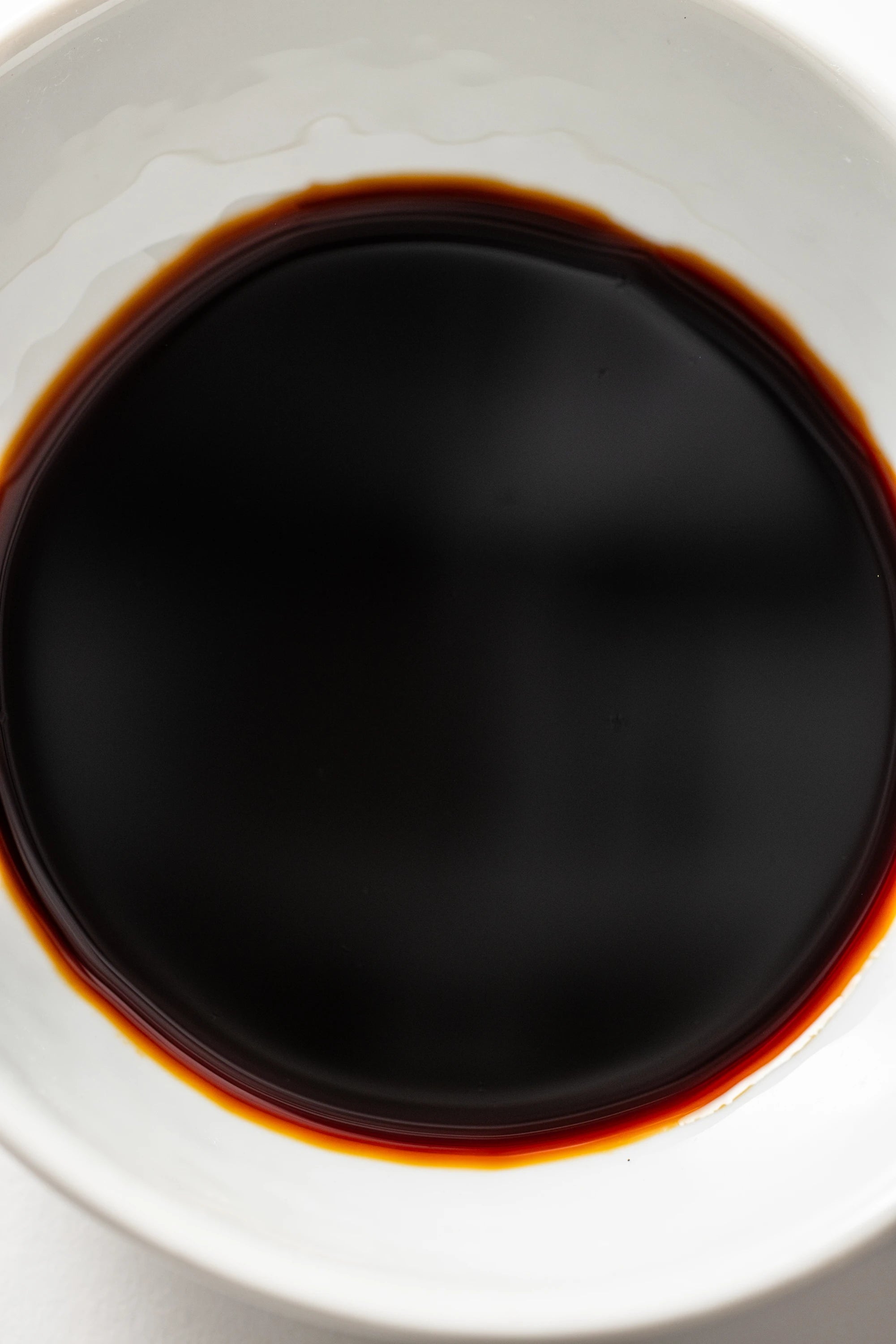 A white ceramic bowl filled with a dark, glossy liquid identified as Matsuai 10‑Year‑Aged Soy Sauce, showing a deep brown‑black color with a warm reddish tint around the edges.