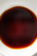 A white bowl filled with Matsuai Marudaizu Koikuchi Soy Sauce, showing a deep, glossy brown liquid with a slightly lighter ring around the edge where it meets the bowl.