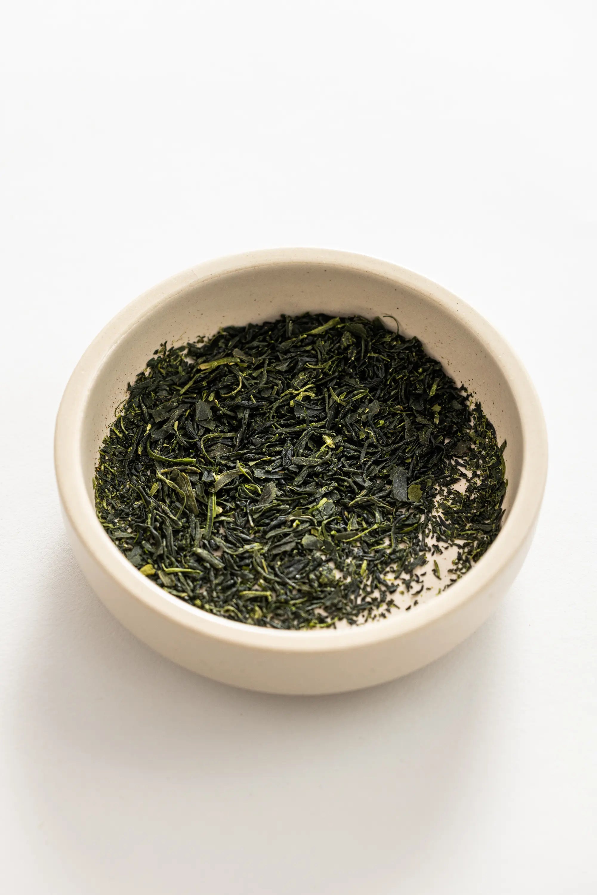 Bowl of green Oyama Seicha Yabukita Sencha tea leaves on a white background