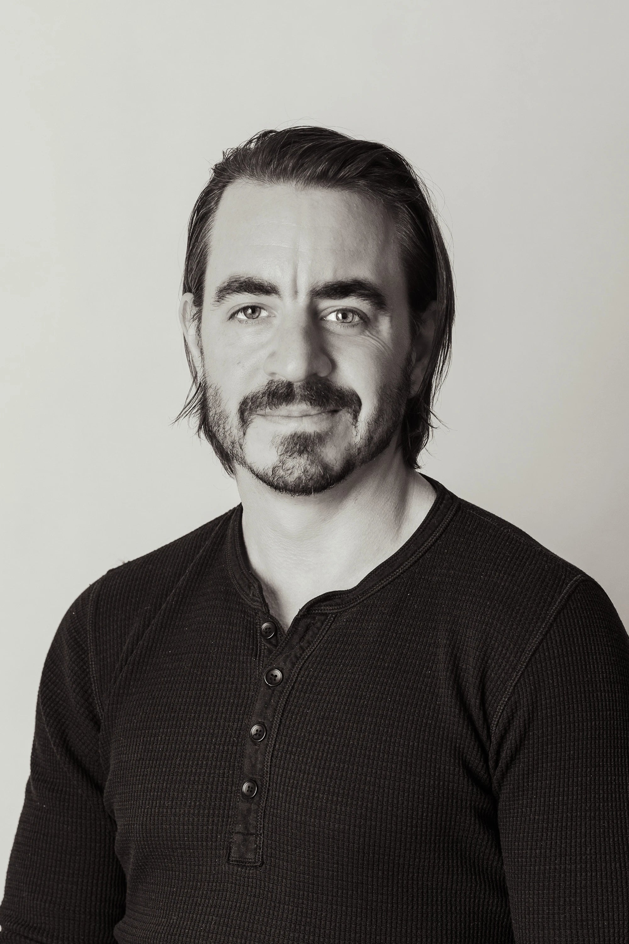 Black and white portrait of a man with tattoos on his arms wearing a dark long-sleeve shirt.