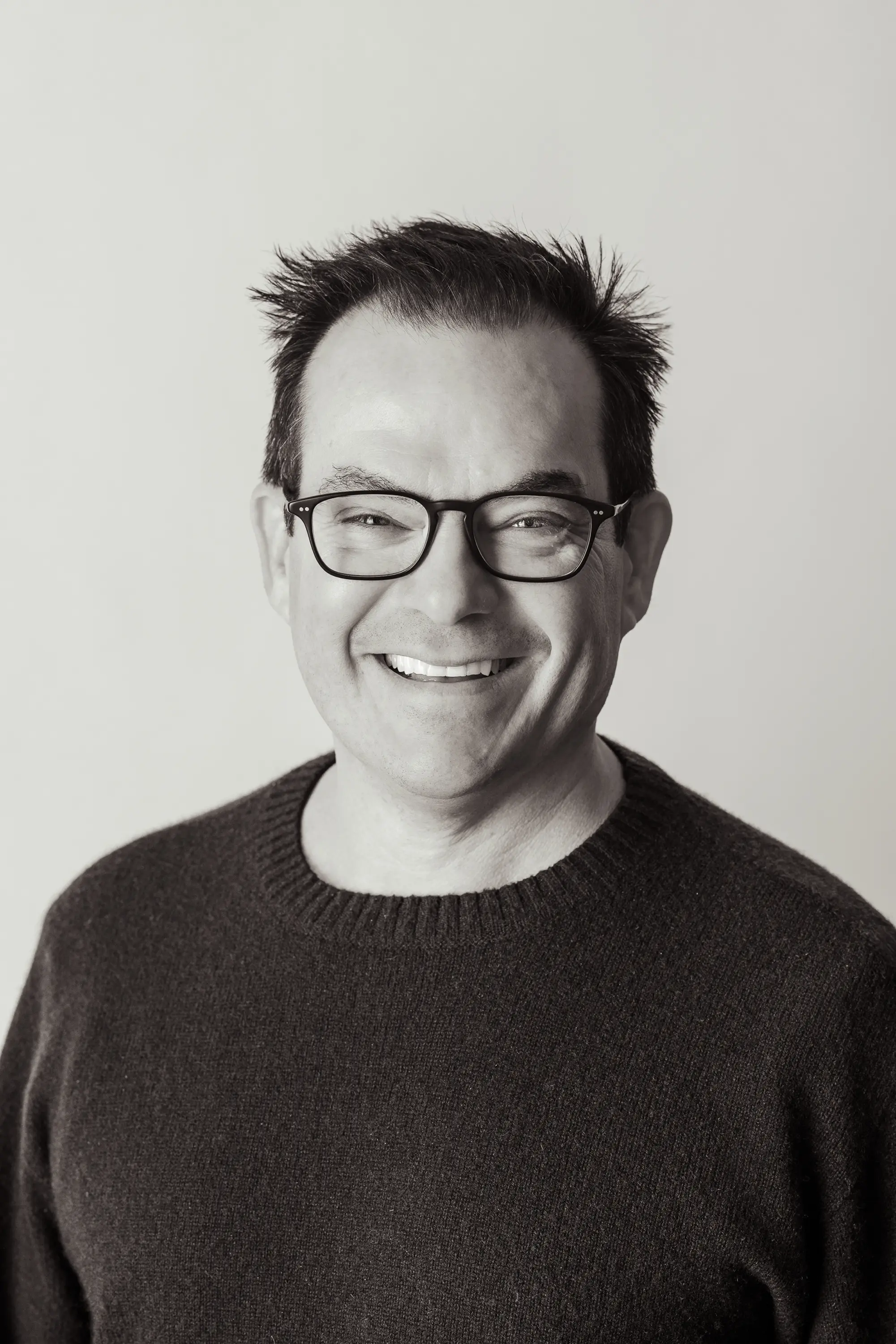 Black and white portrait of a man wearing glasses and a sweater against a plain background