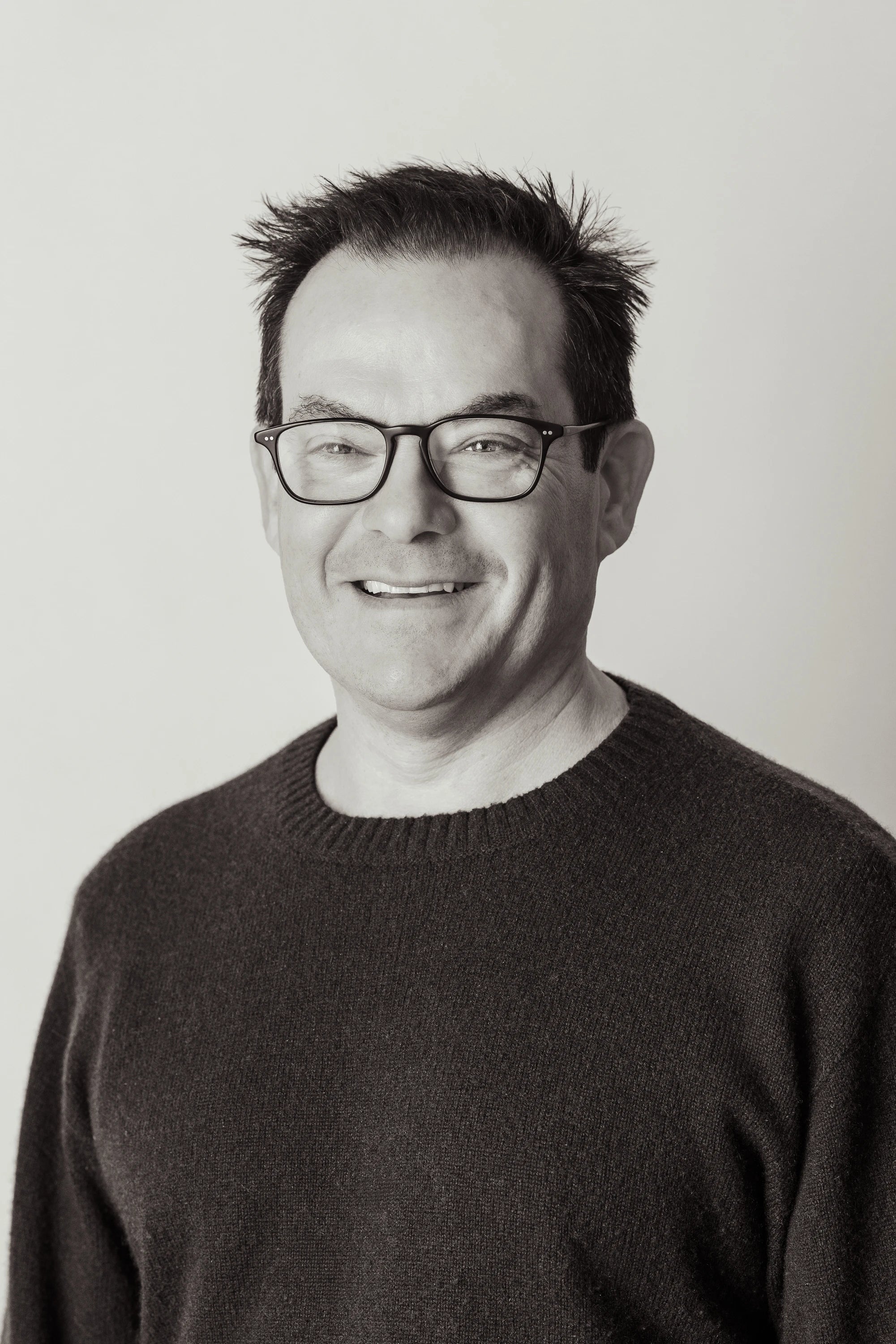 Black and white portrait of a man wearing glasses and a dark sweater against a plain background