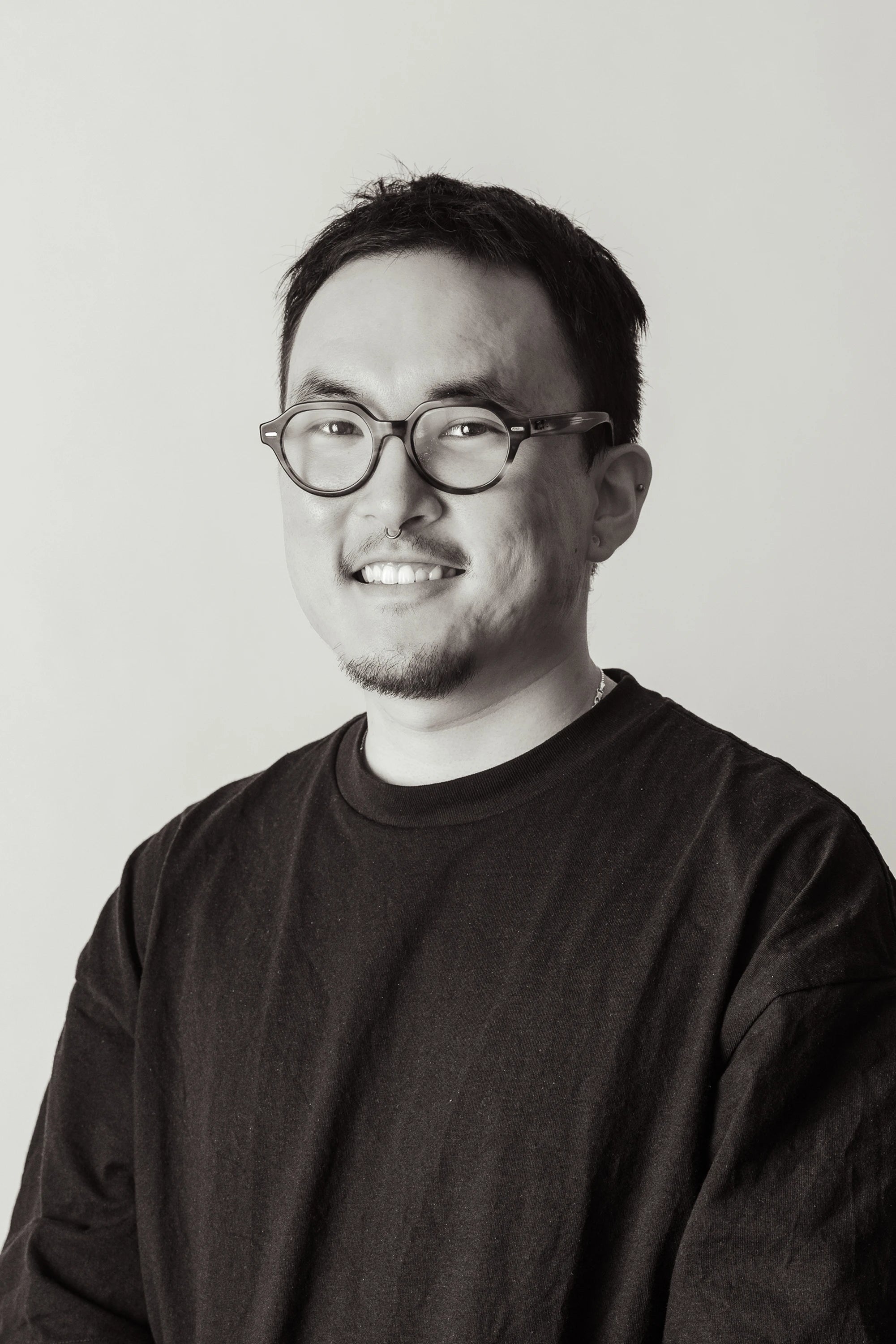 Black and white portrait of a person wearing glasses and a black t-shirt against a plain background