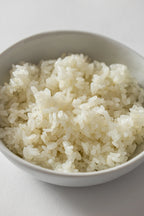 White bowl filled with cooked white rice on a light gray background