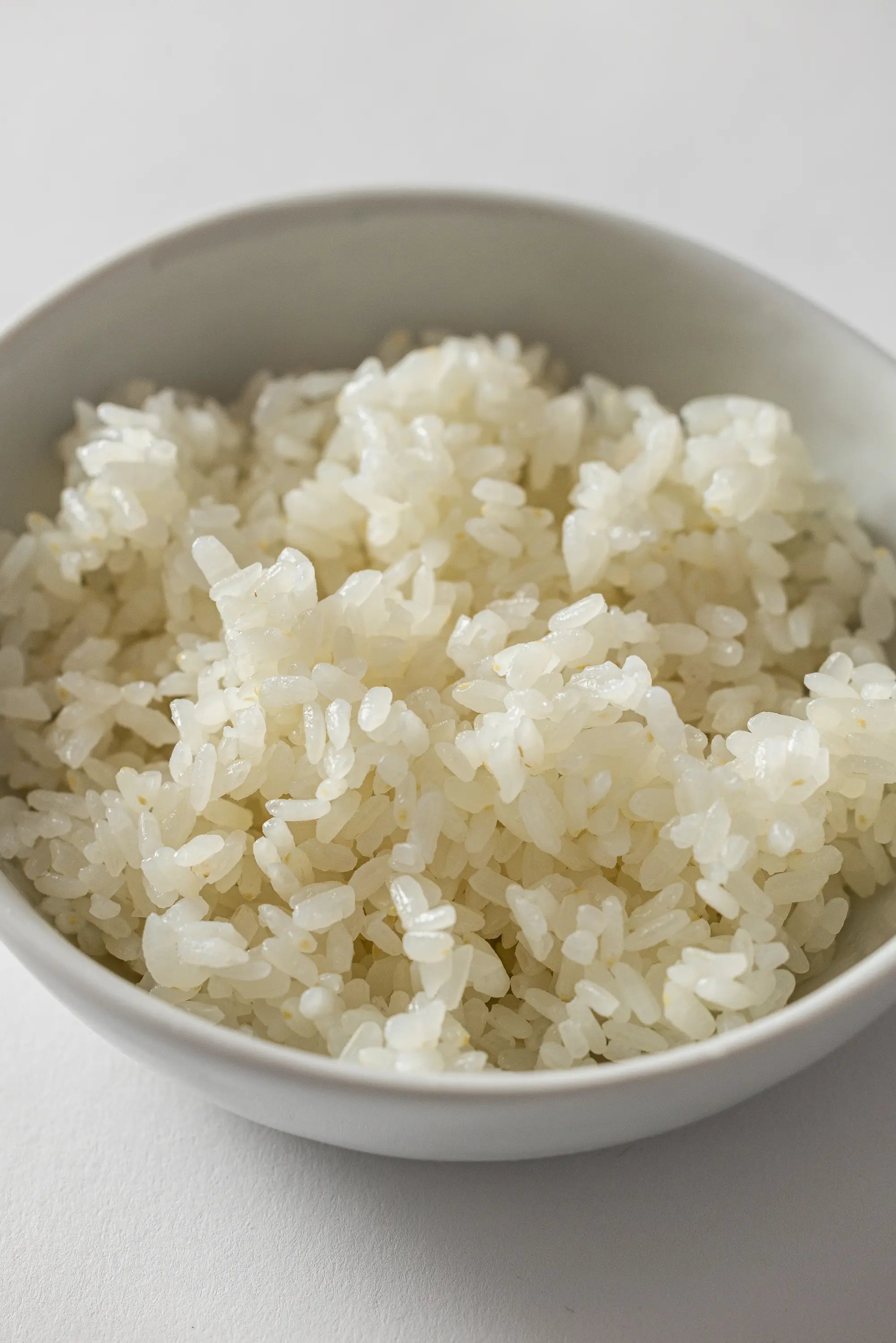 White bowl filled with cooked white rice on a light gray background