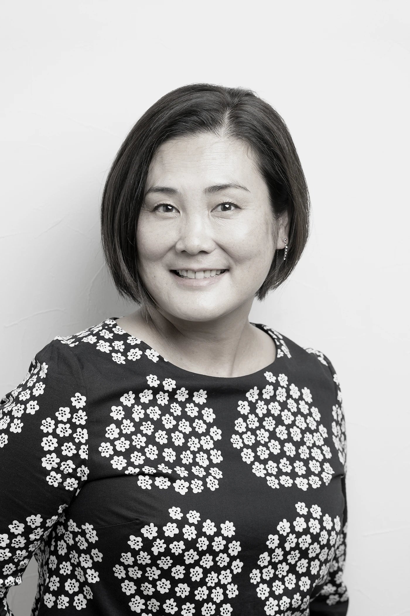 Black and white portrait of a woman wearing a floral dress against a plain background