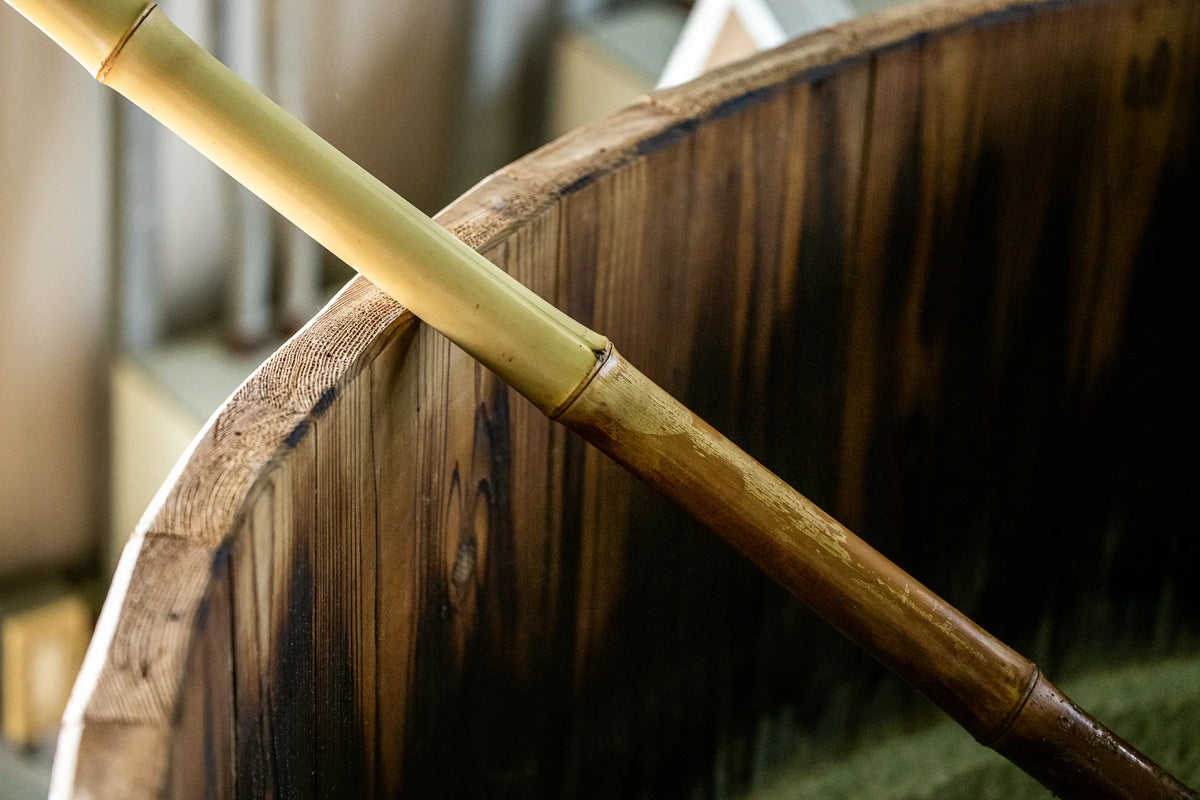 A close-up of a traditional wooden kioke barrel with a bamboo pole resting diagonally across the rim