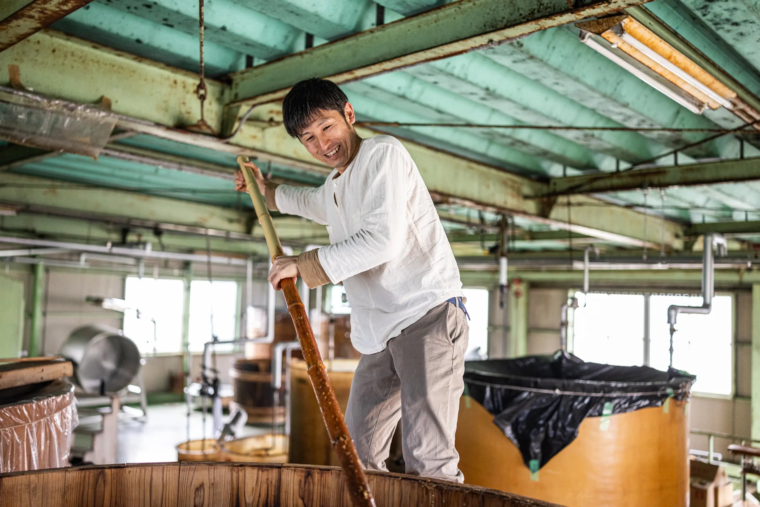 Person stirring a large wooden vat in a factory setting