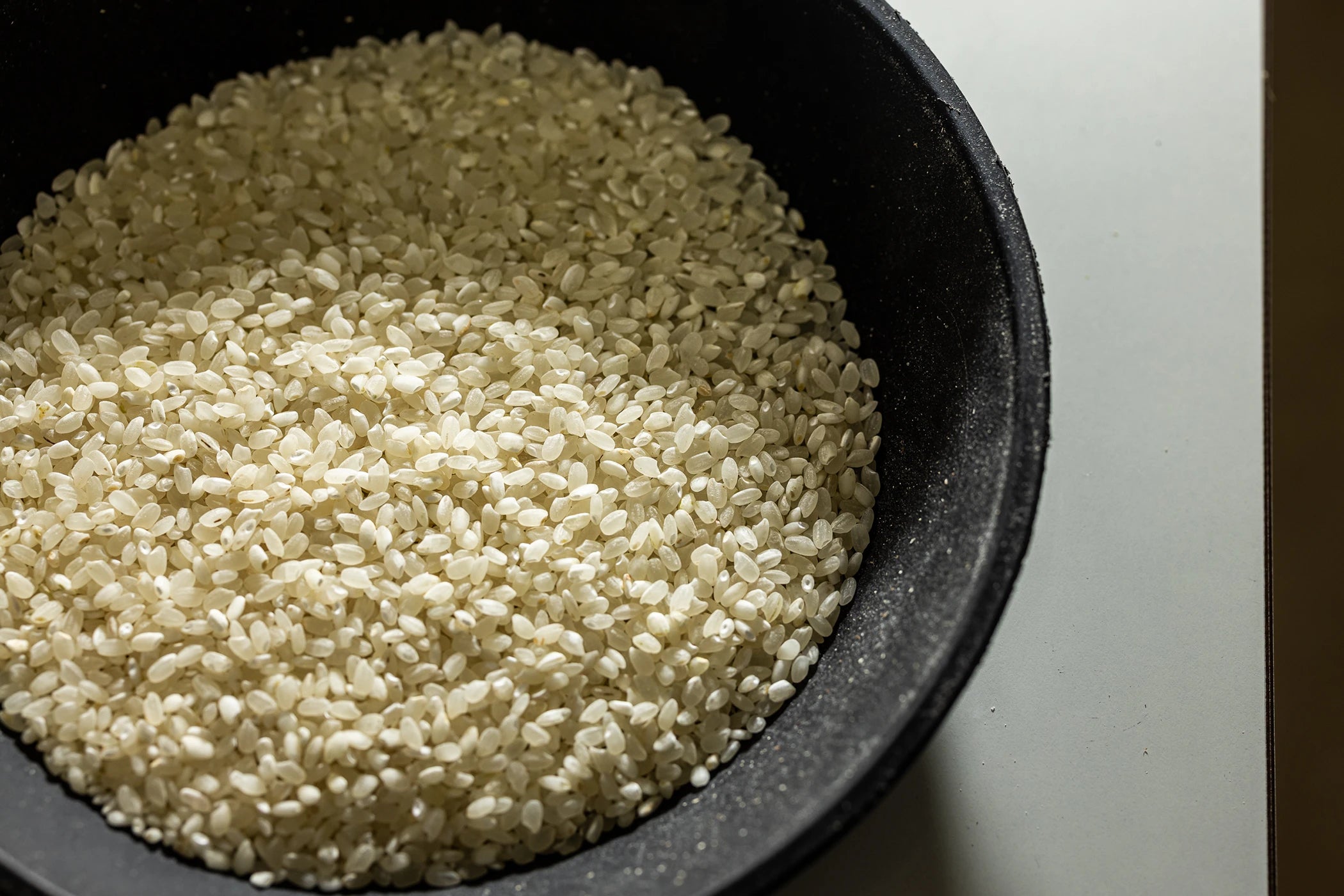 Koshihikari rice uncooked in a black bowl, showing the polished pearlescent short grains.