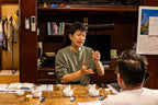 Oishi-san and Henry engaged in a conversation at a table with tea sets in a room.