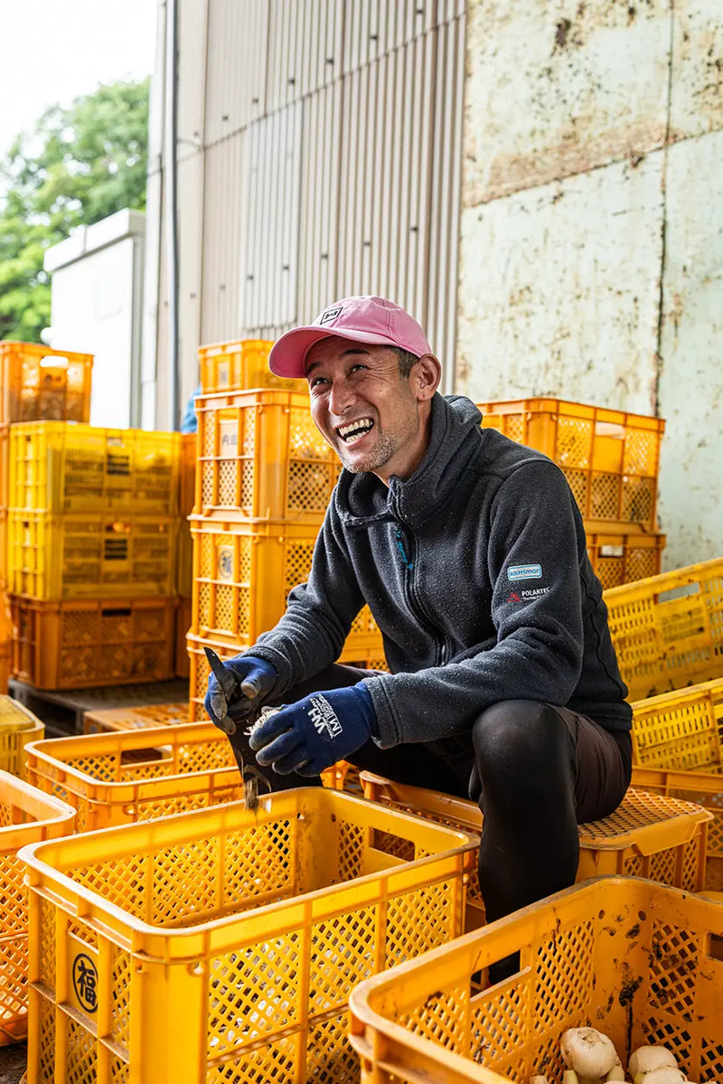 Man in a gray jacket and pink cap among yellow crates, laughing outdoors.