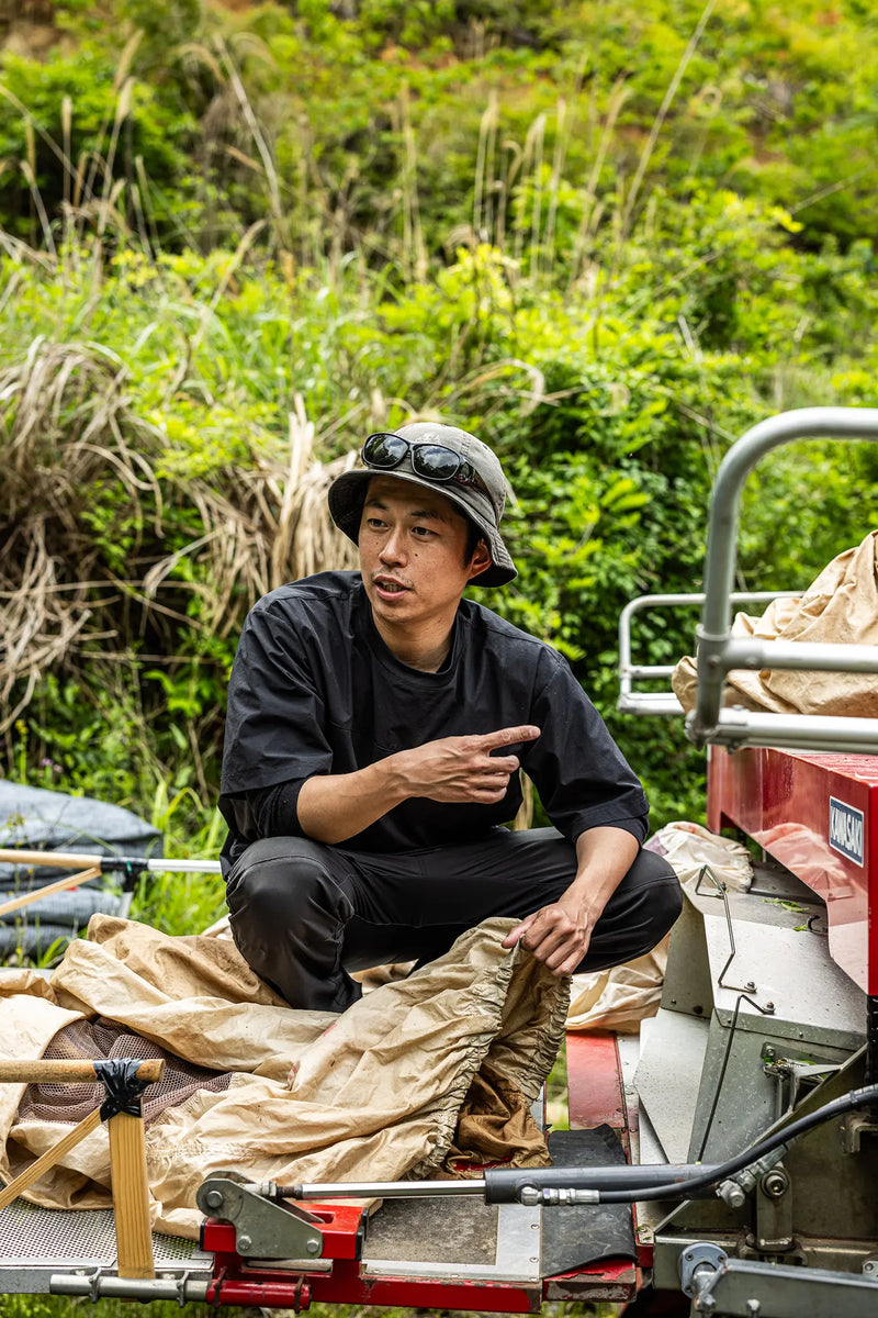 Man sitting on a vehicle in a natural setting, surrounded by greenery.