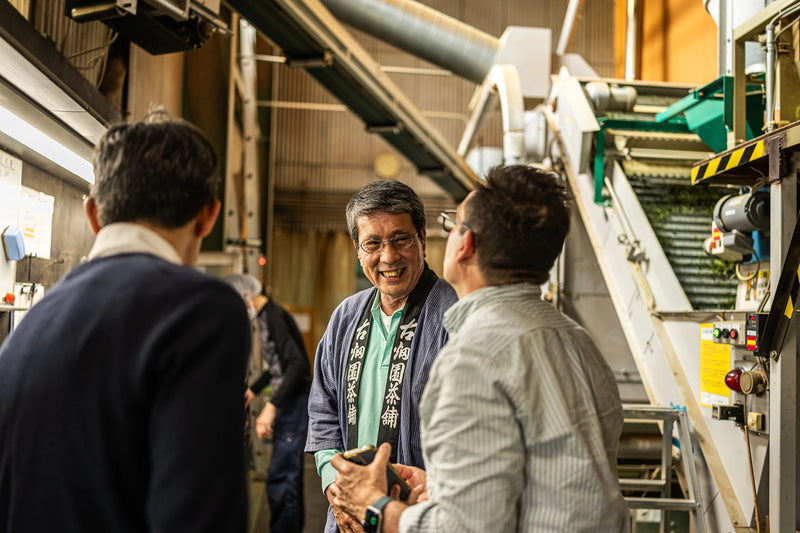 Oyama Seicha tea master in a happi coat greeting a Shokuya visitor inside the tea processing factory.