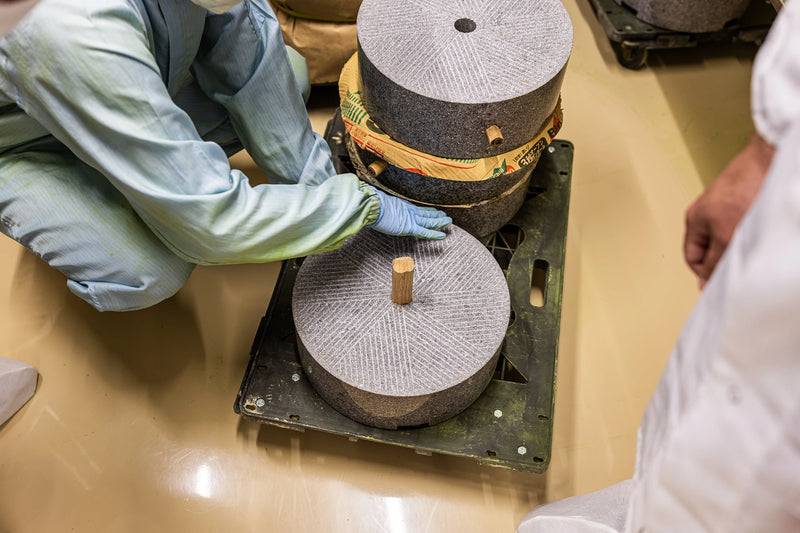 Stone mill being assembled by gloved hands for traditional matcha grinding process.