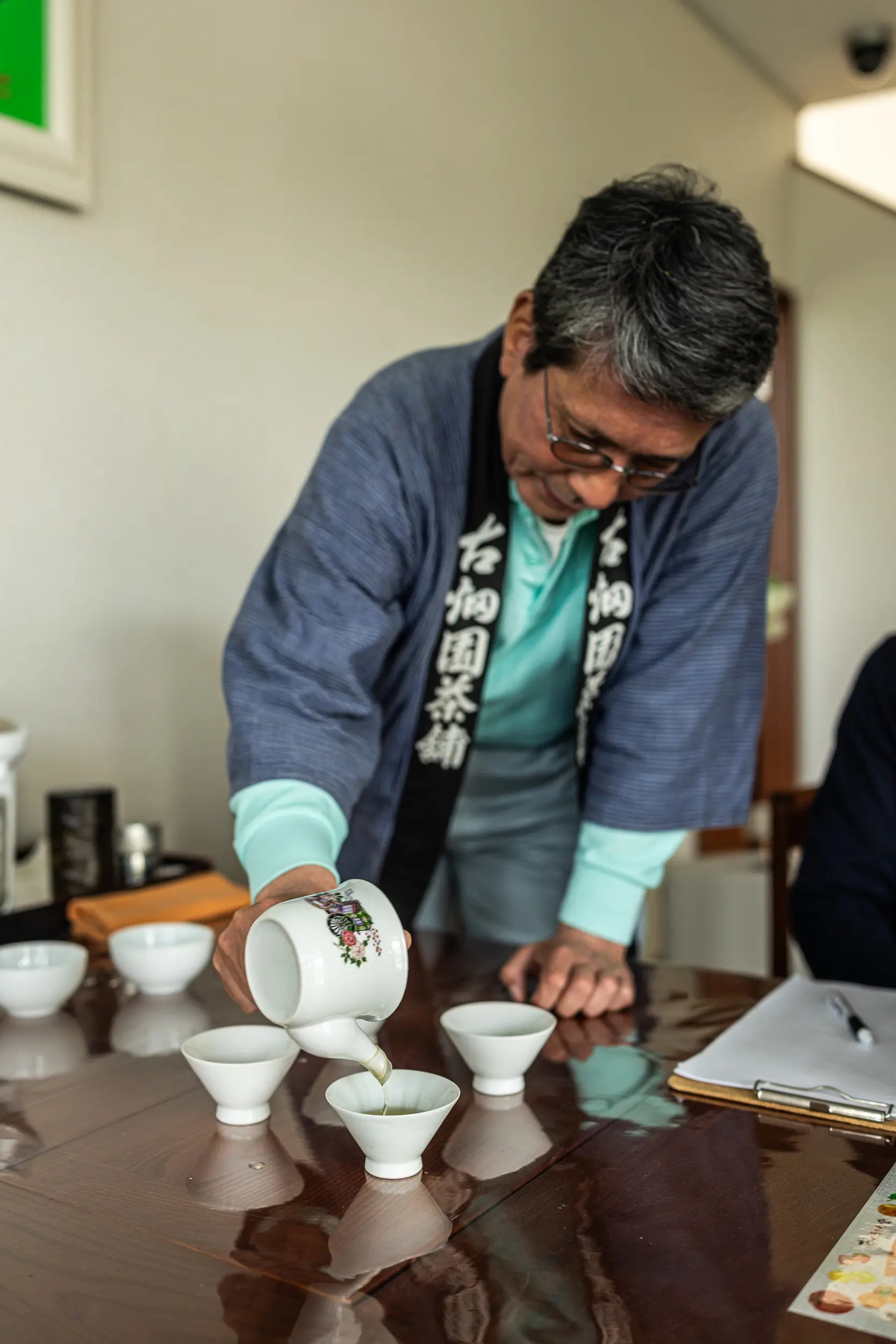 Man performing a tea ceremony with cups on a reflective surface.