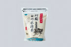 Transparent bag of Kanegae Aso Shirakawa rice on light gray background with Japanese characters on front