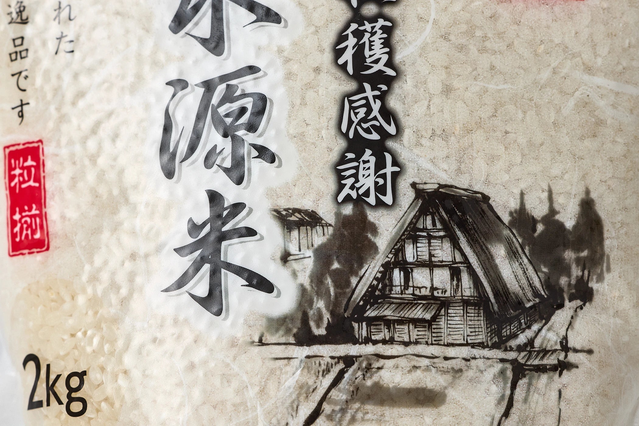 Closeup of design of a house on transparent bag of Kanegae Aso Shirakawa rice on light gray background with Japanese characters on front