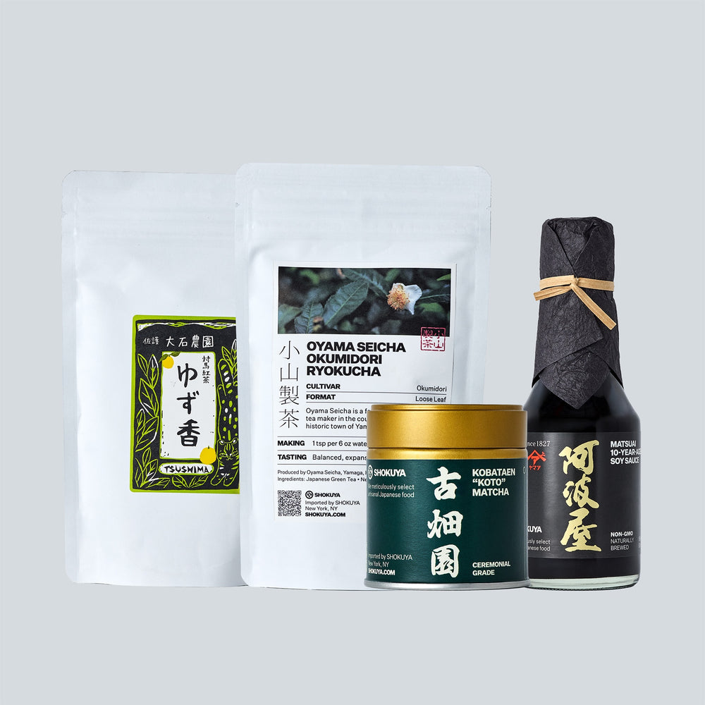 A curated product set featuring a white pouch of tea, a white pouch of Okumodori Ryokucha, a dark green tin of Matcha, and a black bottle of Soy Sauce, arranged on a light gray background.