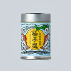 Small metal canister of Japanese yuzu salt from Oishi Farm centered on a light gray background, with a blue illustrated label showing yuzu fruit, fish, and Japanese text.
