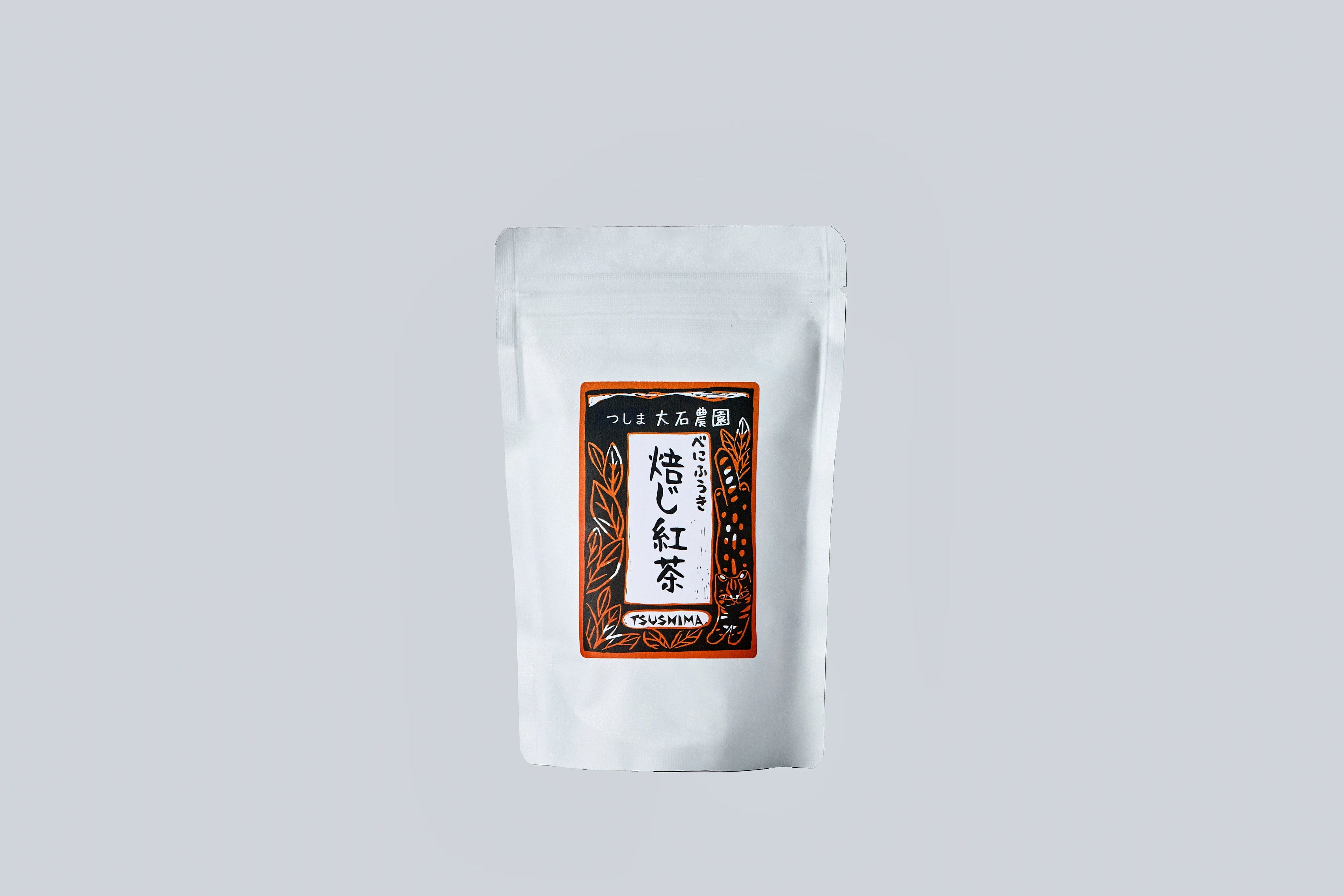 A white resealable pouch featuring a decorative label with Japanese text and illustrations. The label includes stylized tea leaves and reads “つしま 大石農園 べにふうき 焙じ紅茶 TSUSHIMA,” indicating it is roasted black tea from Oishi Farm in Tsushima, Japan.
