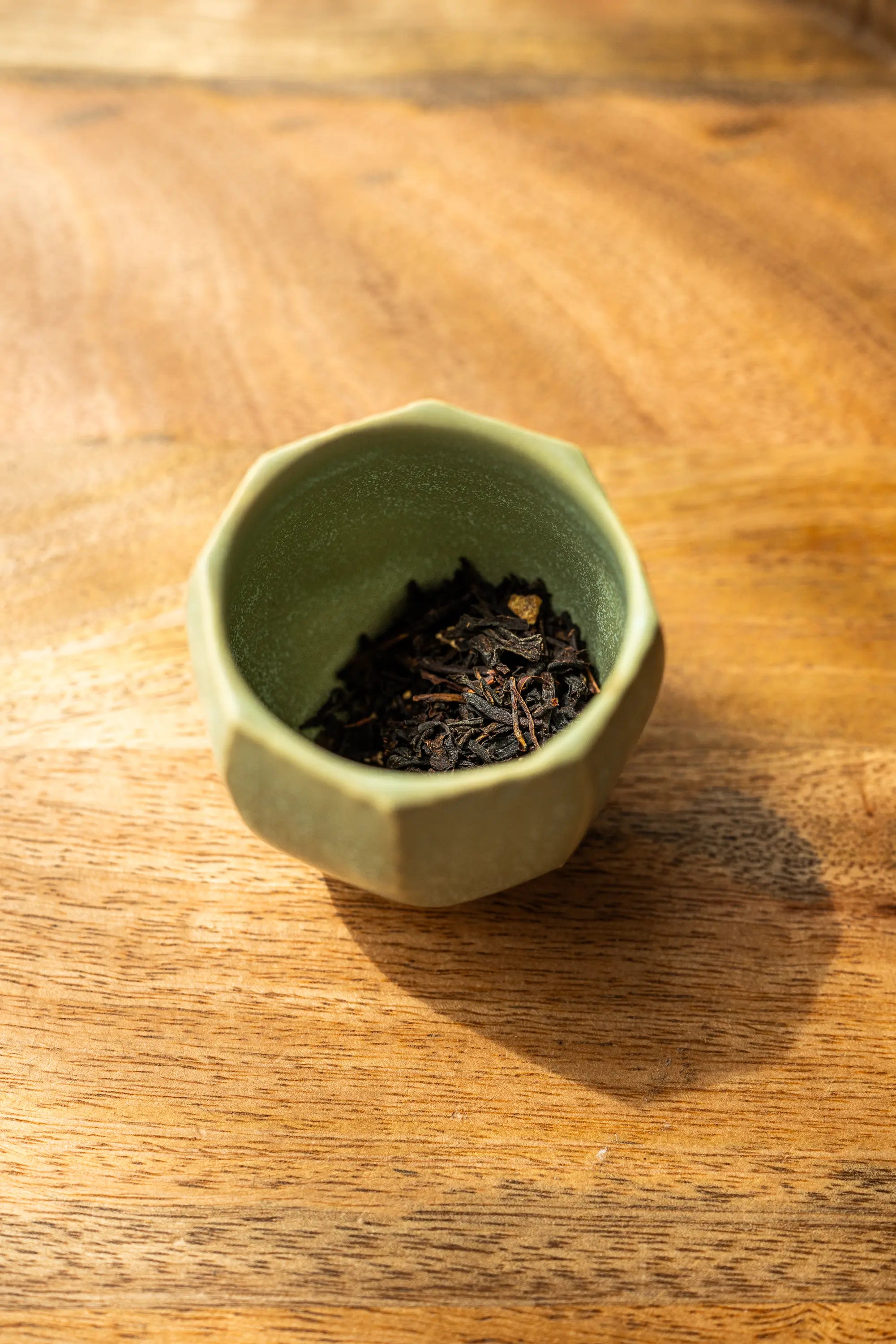 Green ceramic cup filled with tea leaves on a wooden surface